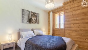 A bedroom with a wooden headboard, a large bed with a dark blanket, two bedside tables with lamps, and a wall-mounted painting of a wolf. - LA Louve - Hauteluce-les-saisies (HAUTELUCE LES SAISIES)