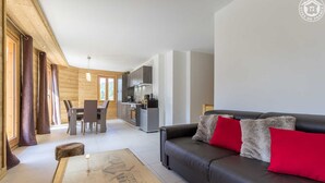 A modern living room with a sofa, a dining table, and a kitchen in the background. - LA Louve - Hauteluce-les-saisies (HAUTELUCE LES SAISIES)