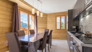 A wooden interior with a dining table and chairs, a kitchen with modern appliances, and large windows offering a mountain view. - LA Louve - Hauteluce-les-saisies (HAUTELUCE LES SAISIES)