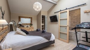 Ein Schlafzimmer mit Bett, Nachttischlampen, Laufband, Fernseher und Schiebetürenschrank.