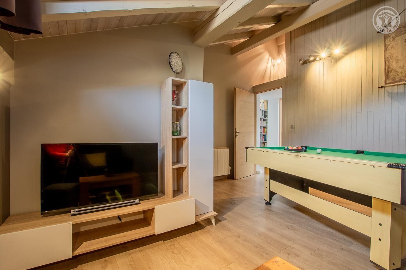 Ein Zimmer mit Fernseher, Regalen und einem Kicker.