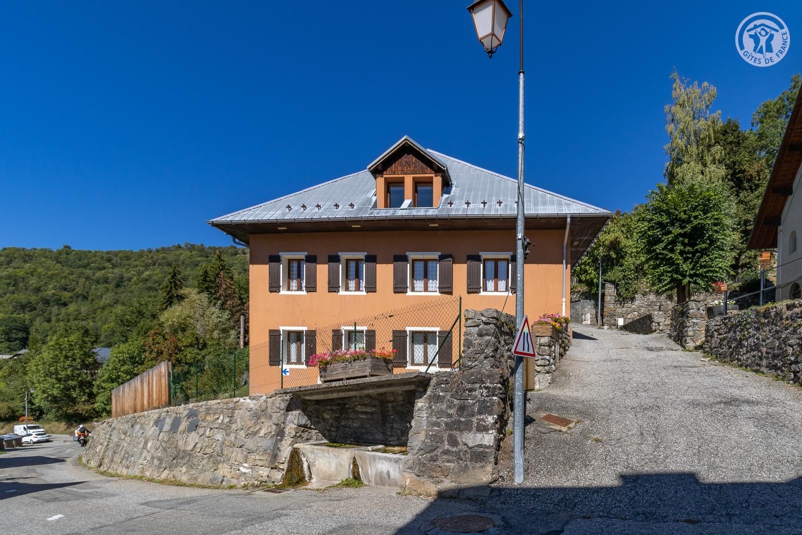 A two-story building with a sloped roof, a stone wall, and a street lamp.