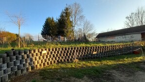 Un área cercada con palets de madera apilados, un letrero que indica estacionamiento y un edificio con techo inclinado al fondo.