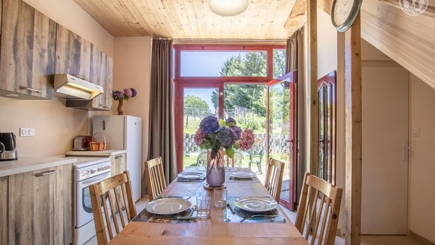 Una mesa de comedor de madera con sillas, un florero y vistas al exterior a través de grandes ventanales.