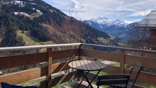 Una terraza de madera con una mesa y sillas que da a un paisaje montañoso con picos nevados.