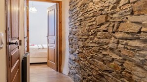 Un pasillo con suelo de madera, paredes de piedra y una cama al fondo.