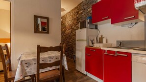 Una cocina compacta con armarios rojos, un refrigerador blanco y una mesa de comedor de madera con mantel estampado.