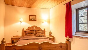 Een houten bed met een hoofdeinde in de vorm van een hart, twee bedlampen, een klein nachtkastje en een raam met een rode gordijn.
