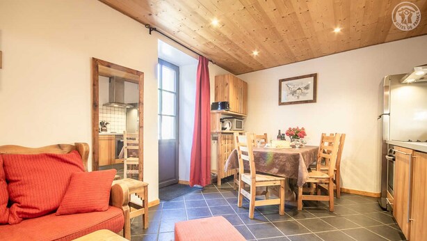 Een gezellige woonkamer met een bank en een salontafel, een eethoek met een tafel en stoelen, en een keuken met houten kastjes en apparatuur.