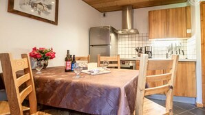Een eetgedeelte met een tafel voor vier personen, houten stoelen, een bloevas en flessen wijn.