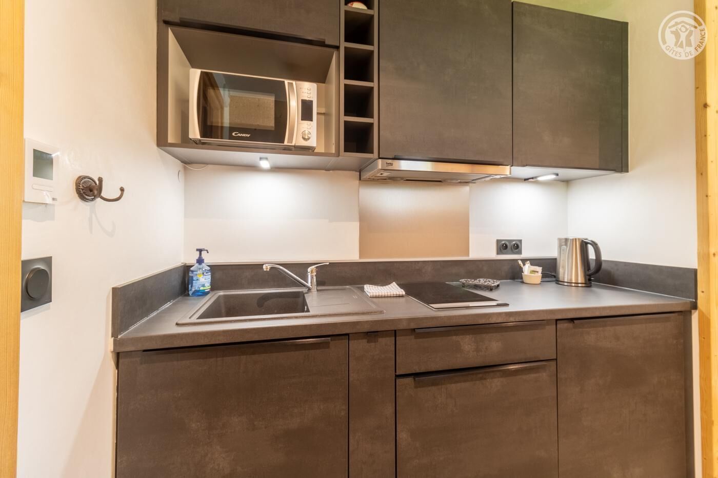 A modern kitchen with a built-in microwave, stainless steel sink, and a kettle on the counter.