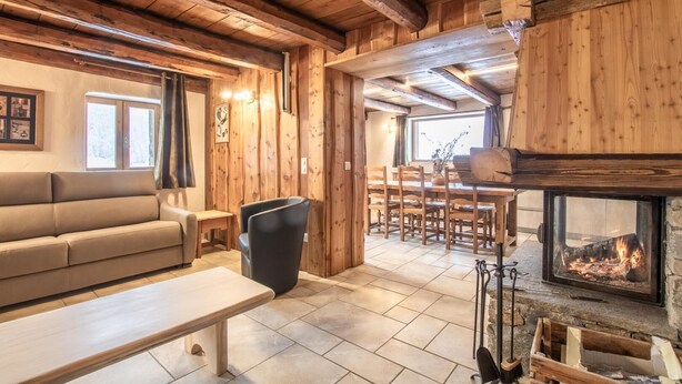 Ein gemütliches Blockhaus mit Holzeinrichtung, Kamin, einer Couch, einem Esstisch und Stühlen.
