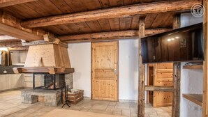 Ein rustikaler Innenraum mit Kamin aus Stein, Holzbalken und einer Holztür.