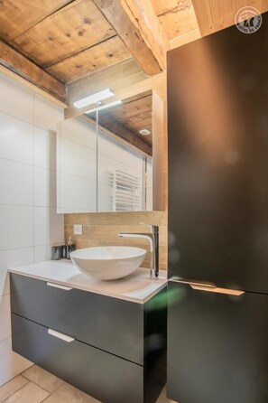 Ein modernes Badezimmer mit einem großen Spiegel, einem Aufsatzwaschbecken und einem schwarzen Schrank.