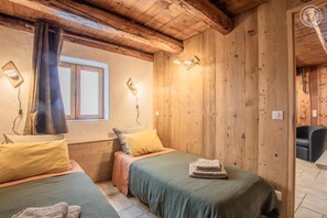 Ein gemütliches Zimmer mit zwei Betten, Holzwänden, einem Fenster und einem Sessel.