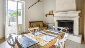 Een gezellig eetgedeelte met een houten tafel, witte stoelen en decoratieve placemats. Een in de muur gebouwde open haard, en boven hangt een rustieke decoratie van een trident.