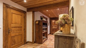Un couloir en bois avec un sol carrelé, des portes en bois et un meuble en bois orné d’un vase de fleurs.