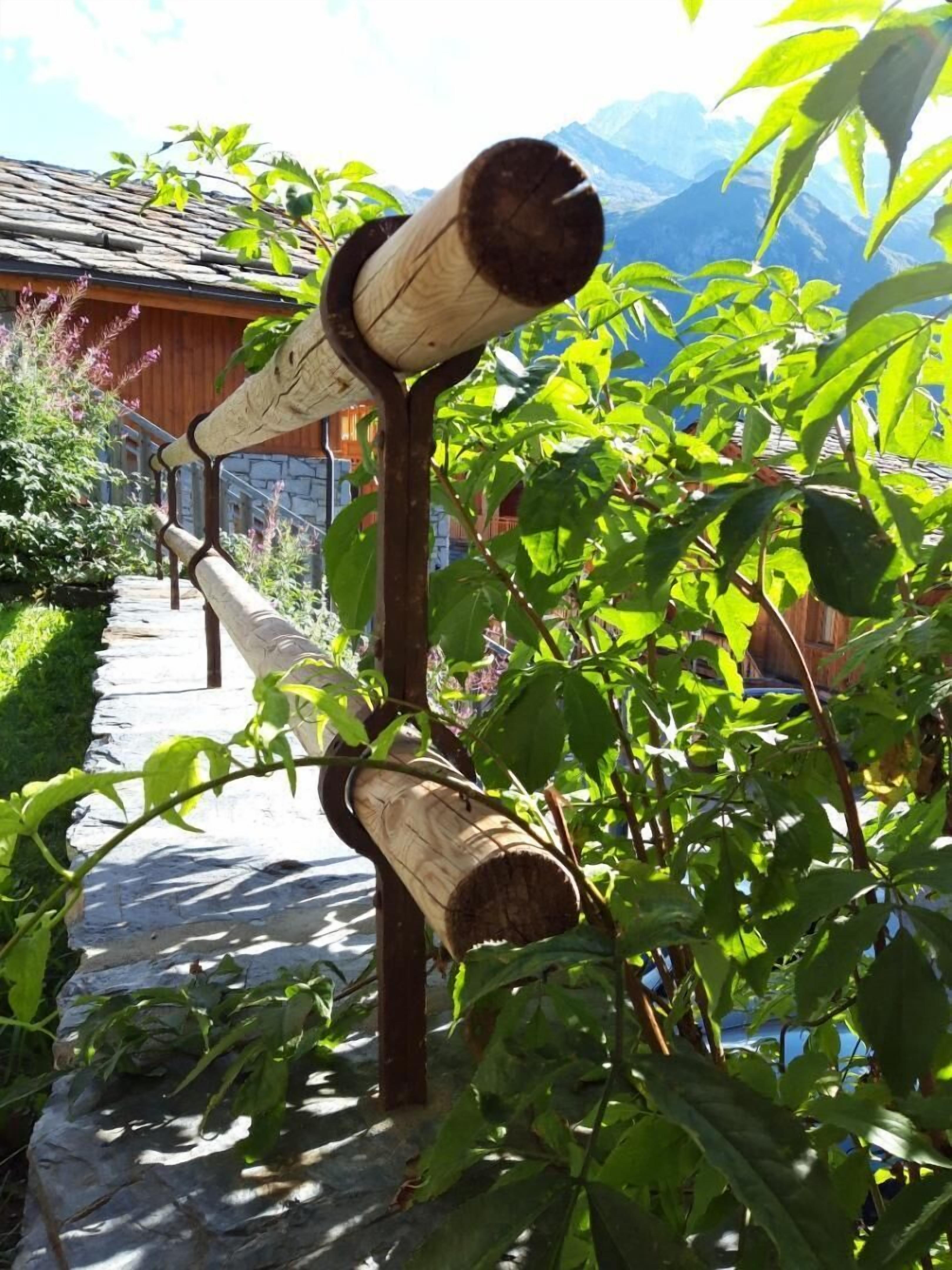 Une structure en bois, faite de troncs d’arbres, entourée de verdure et bordée d’un sentier en pierre.