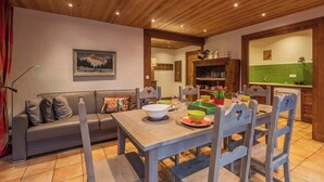 Un coin repas accueillant, avec une table en bois dressée pour quatre personnes, entourée de chaises en bois. Un canapé avec des coussins est placé contre le mur, et un tableau est accroché au-dessus.