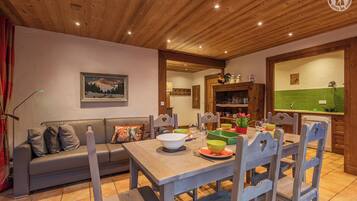 Un coin repas accueillant, avec une table en bois dressée pour quatre personnes, entourée de chaises en bois. Un canapé avec des coussins est placé contre le mur, et un tableau est accroché au-dessus.