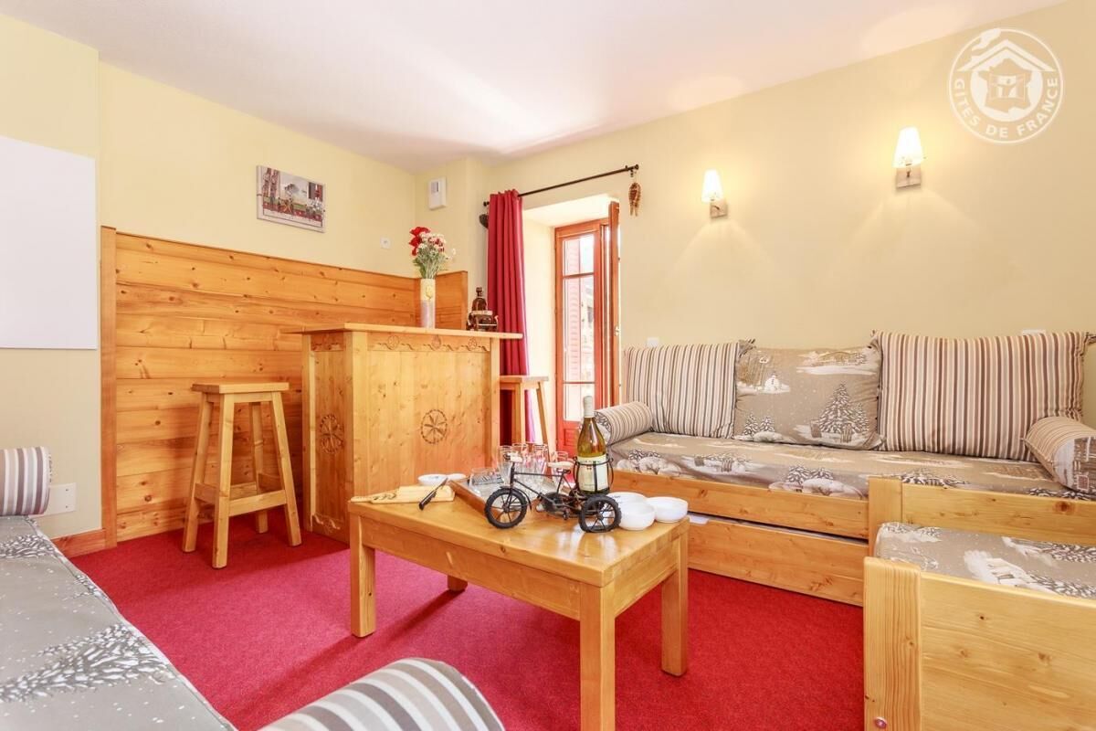 Un salon chaleureux avec un mur en bois, un canapé orné de coussins à rayures, une table en bois sur laquelle sont posés un vélo et une bouteille, et un tapis rouge.