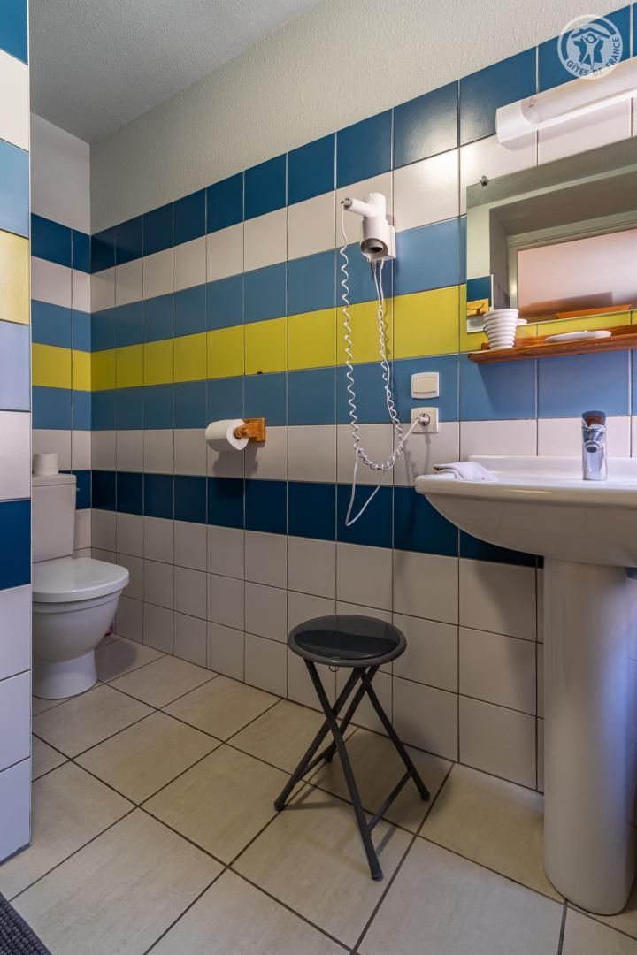 Een badkamer met toilet, wastafel, haardroger en een klein krukje.