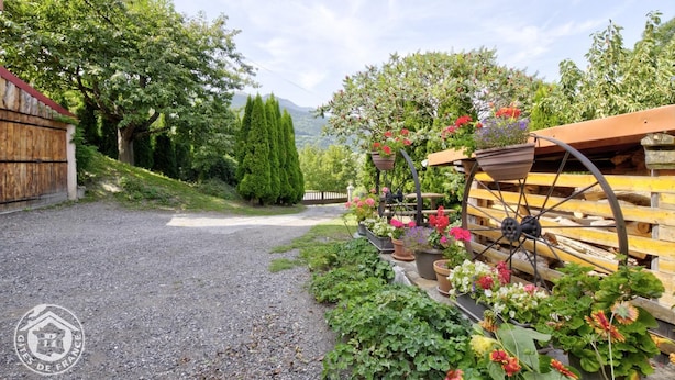 A gravel driveway leading to a wooden structure with a metal wheelbarrow and flower pots. - Gite LES Emptes - Aigueblanche (AIGUEBLANCHE)