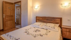 A bedroom with a wooden bed, floral bedding, and two wall-mounted light fixtures. - Gite LES Emptes - Aigueblanche (AIGUEBLANCHE)