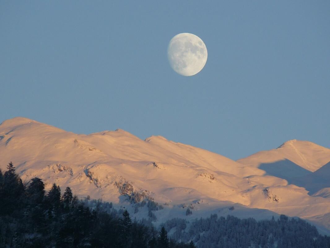 Paisaje montañoso con una luna llena en el cielo.