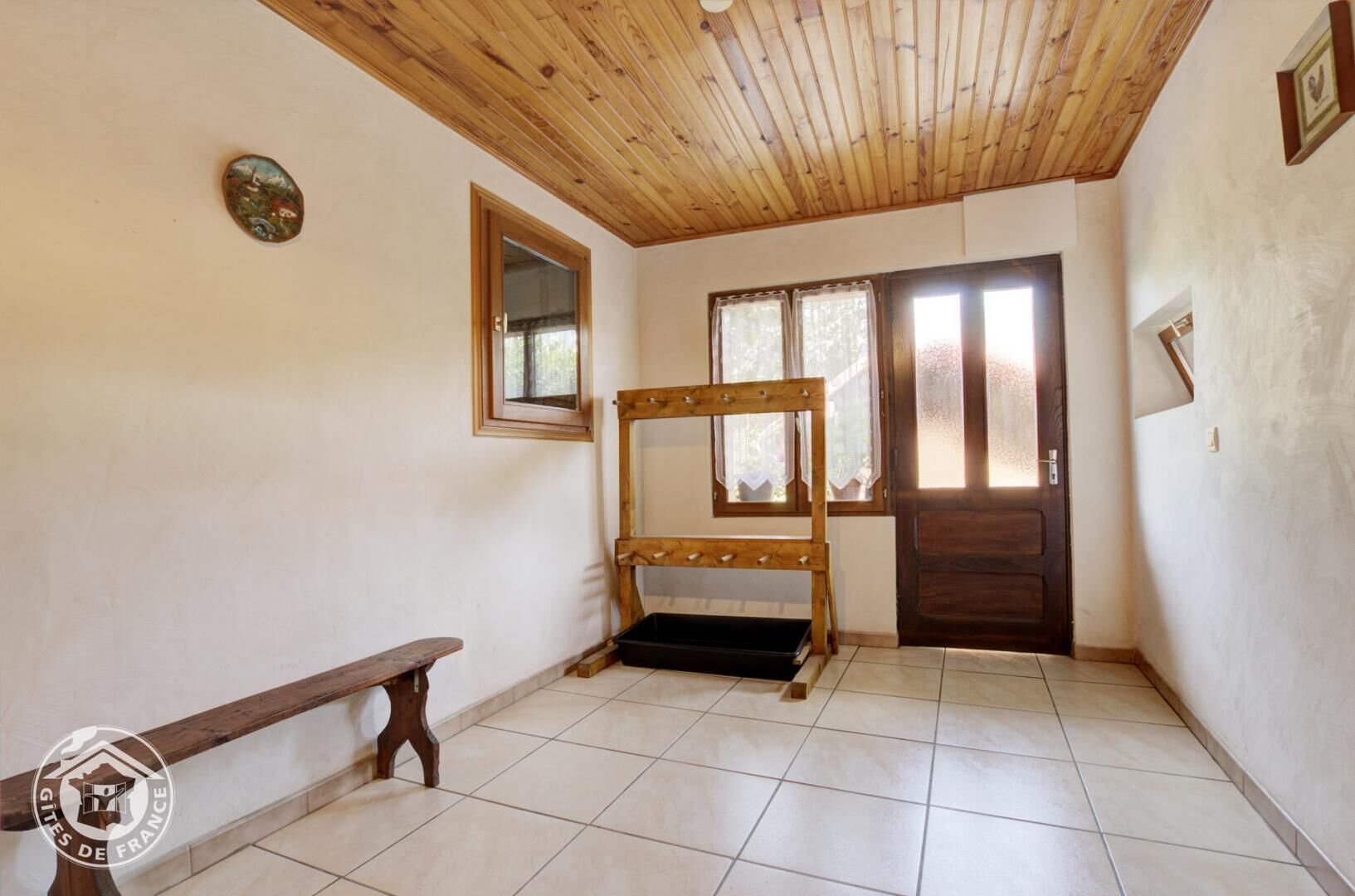 A room with a wooden bench, a wooden ladder, a door, and a window with curtains.