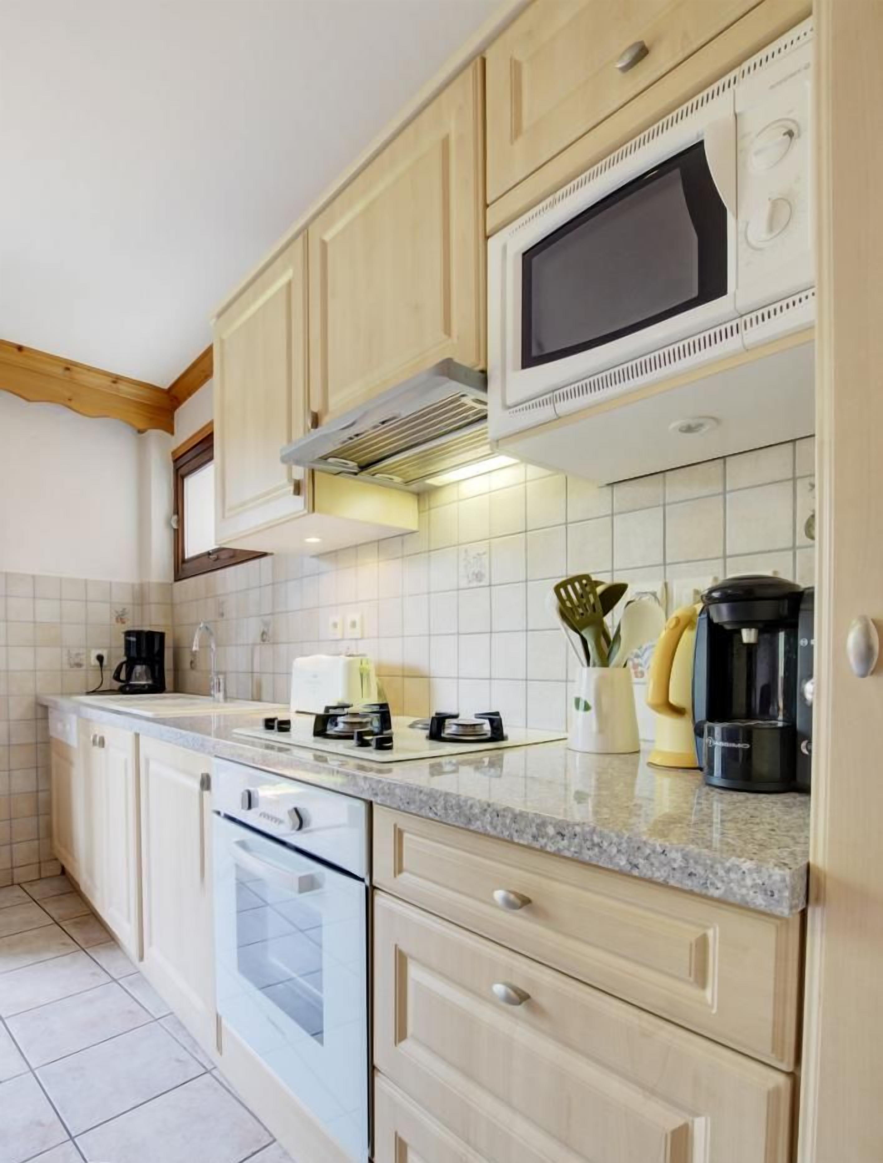 A kitchen with light wooden cabinets, a microwave, a stove, and a coffee maker.