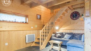 L’intérieur d’un chalet en bois chaleureux et accueillant, avec un escalier, un canapé, une petite table et une horloge au mur.