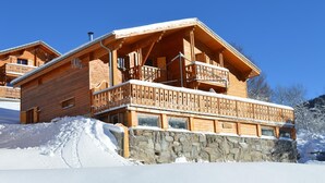 Un chalet en bois, avec des fondations en pierre, des balcons en bois et un paysage enneigé.