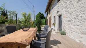 An outdoor patio with a wooden table and chairs, a stone wall, and a small garden area. - Chez LA Philo - Nances (NANCES)