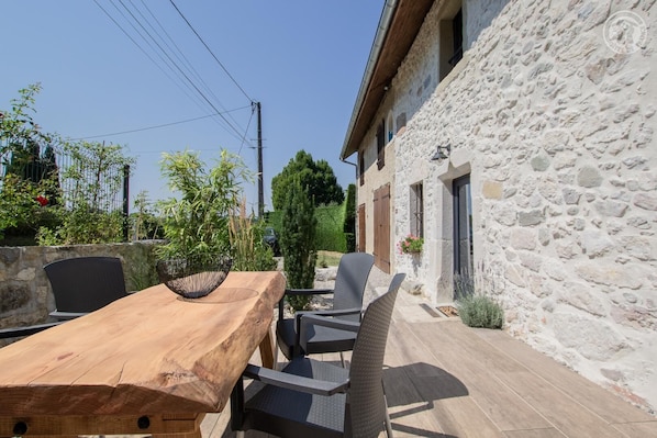 An outdoor patio with a wooden table and chairs, a stone wall, and a small garden area.