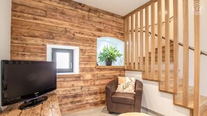 A modern living room with a wooden wall, a flat-screen TV, a comfortable armchair, a small table, and a staircase. - Chez LA Philo - Nances (NANCES)