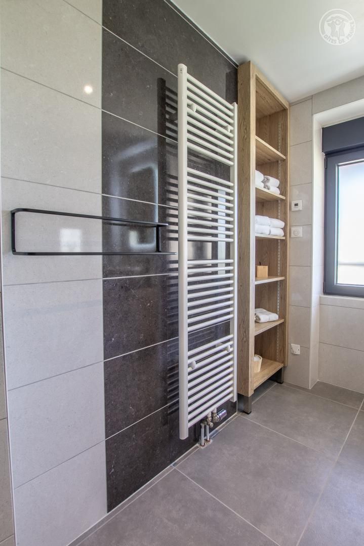 Un baño moderno con un toallero integrado, una estantería de madera y un ventanal que proporciona luz natural.