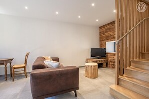 A modern living room with a brown sofa, a wooden TV stand, a small round table, and a staircase with a wooden railing.