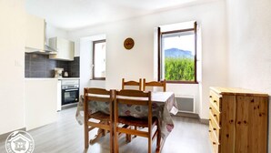 A modern kitchen with a dining area, a view of greenery through a window, and a wooden cabinet.