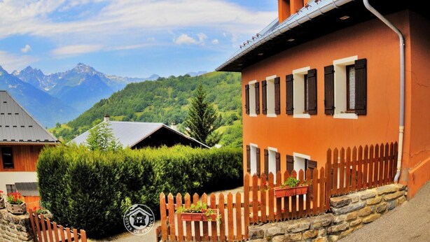 A traditional chalet with a stone foundation, wooden shutters, and a stone fence.