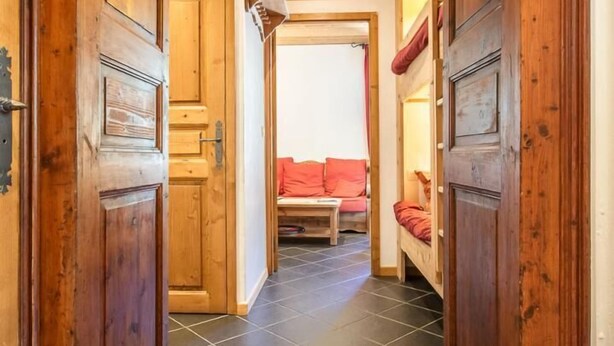 Un couloir avec des portes en bois et un sol carrelé qui mène à une pièce contenant un lit et un canapé rouge.