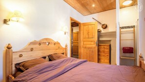 Une chambre à coucher avec un lit en bois, deux lampes fixées au mur et une armoire sur laquelle est accrochée une serviette.