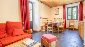 Un salon chaleureux avec un canapé rouge, une table à manger en bois et des chaises, ainsi qu’un coin cuisine doté de placards.