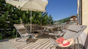 Une terrasse extérieure avec une table en bois, deux chaises et un grand parasol.