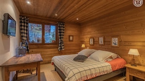 A cozy wooden cabin bedroom with a bed, a desk, and a window with curtains. - Chalet Chaudanne - LO Soli (SAINTE FOY TARENTAISE)