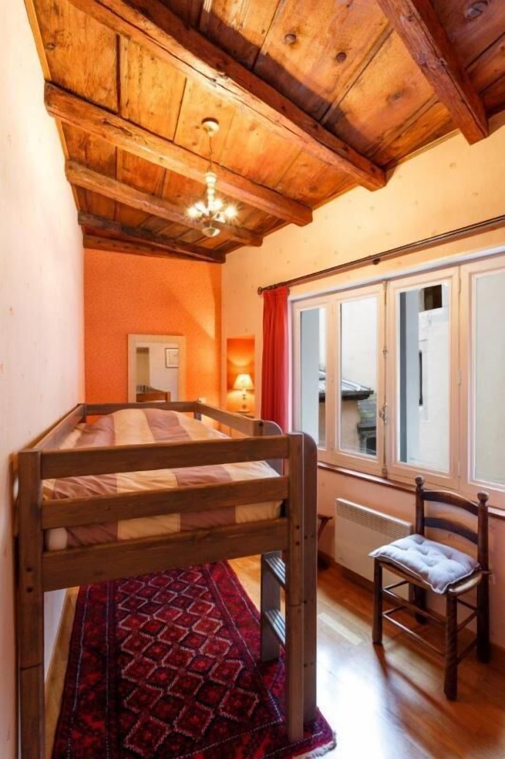 Une petite pièce agréable, dotée d’un lit superposé, d’une chaise, d’une fenêtre avec des rideaux et d’un radiateur.