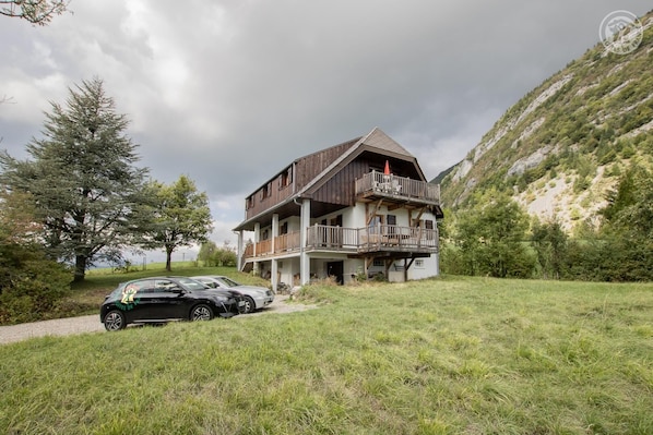Situated in a grassy area with a mountain backdrop, this house features a two-story design with a balcony on the upper floor.