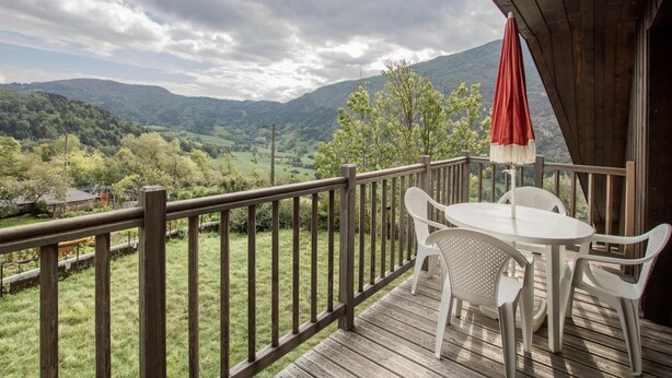 A wooden deck with a table and chairs, overlooking a mountainous landscape.