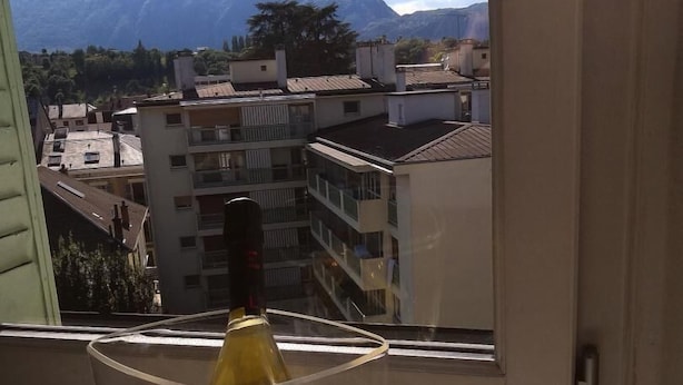 Eine Weinflasche in einem Glas auf einem Fensterbrett mit Blick auf Gebäude und Berge.