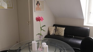 Ein modernes Wohnzimmer mit einem Glastisch, einer schwarzen Ledersofa und einer rosa Blumenvase.